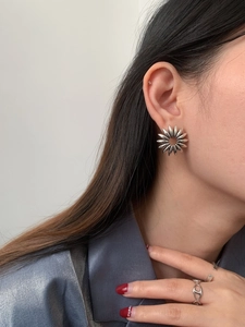 Close-up of a silver hollow sunflower stud earring and matching minimalist rings on a model