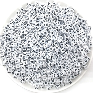 Detailed top view of white 7mm alphabet cube beads piled in a dish for DIY crafts