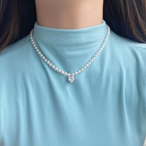 Detailed view of a white pearl necklace with a heart-shaped zircon pendant on a model