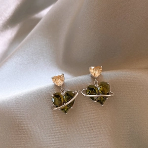 Macro shot of olive green heart zircon planet earrings on grey silk fabric texture