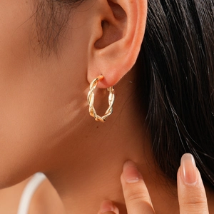 Close-up of golden twisted hoop earring with polished metallic texture on a female model
