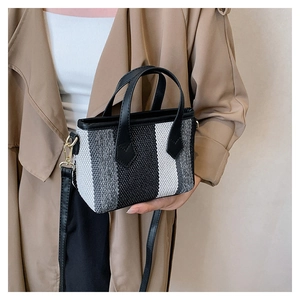 Fashionable striped canvas handbag featuring black leather handles on a trench coat model