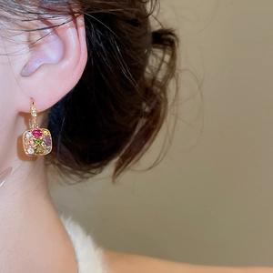 Detailed close-up of gold-plated square earrings with colorful gemstones worn by a model