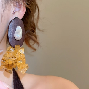 Detail of wooden earring featuring irregular pearls and amber resin beads on a model