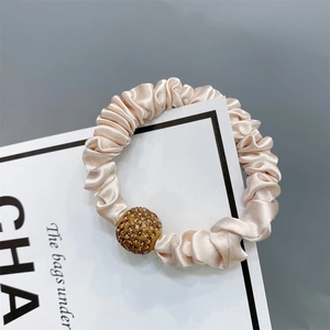 Detail of champagne satin scrunchie featuring a luxury gold rhinestone-encrusted bead