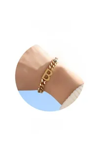 Détail d'un bracelet gourmette plaqué or avec un pendentif lettre B porté au poignet