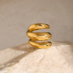 Detail of 18k gold plated triple-layer spiral ring on textured white stone pedestal