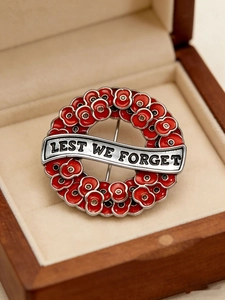 Detailed view of red enamel poppy wreath brooch with Lest We Forget slogan in a gift box