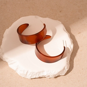 Close-up of vintage amber acrylic C-shaped earrings on a textured stone surface