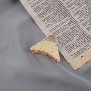 Detail view of a large golden metal hair claw clip with striped texture on a book page