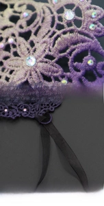 Detailed macro view of purple lace embroidery with shimmering rhinestones and black ribbons