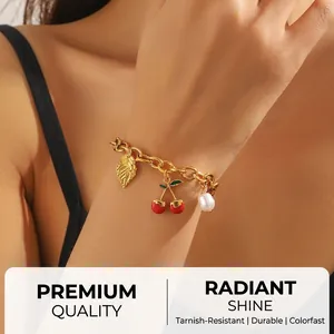 Close-up of gold chunky chain bracelet with leaf, cherry, and pearl charms on wrist