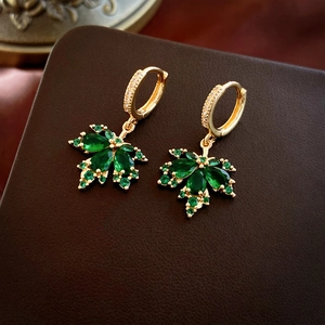 Macro shot of gold-plated maple leaf earrings with emerald green zircon gemstones