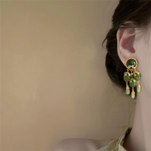 Vintage gold and green tassel earrings with jade-like beads worn on a model's ear