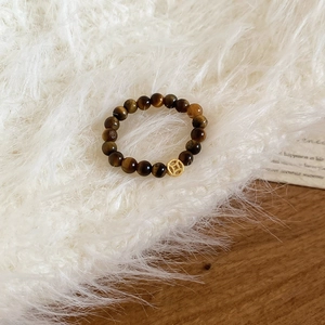 Detail of tiger eye bead ring with a golden coin charm on a soft white plush background