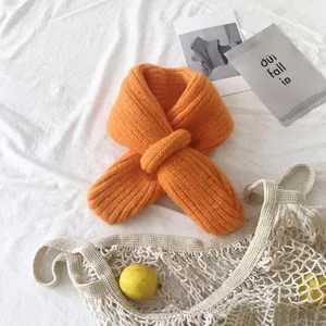 Close-up of orange chunky knit baby neck warmer with a cross-loop design on white cloth