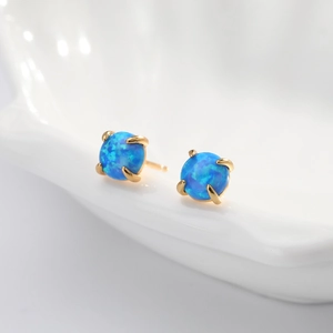 Detail of blue opal stud earrings with gold claw setting on a white ceramic plate