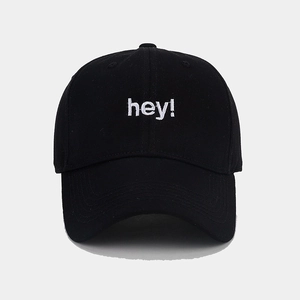 Detailed close-up of white 'hey!' embroidery on a black twill cotton baseball cap