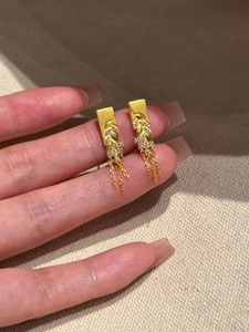 Macro detail of gold-plated wheat-ear tassel earrings with sparkling zircon accents