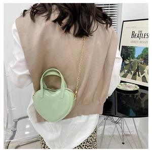 Mint green heart-shaped crossbody bag with gold chain strap shown on person