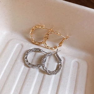 Macro detail of gold and silver twist textured hoop earrings on a beige tray