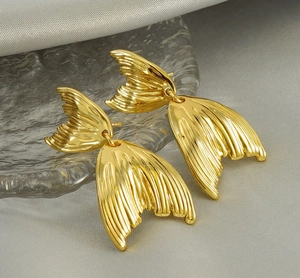 Close-up of 18K gold fishtail stud earrings with brushed metal texture on silk background