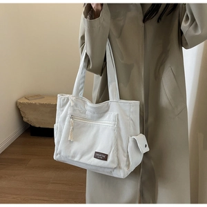 Detail view of white corduroy tote bag featuring multi-pocket design and leather fashion label