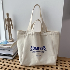 Detail of off-white canvas tote bag with blue lettering on a minimalist wooden seat