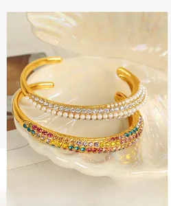 Macro shot of gold C-shaped open bracelets featuring three rows of pearls and colorful zircons