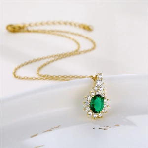 Golden necklace with oval green crystal pendant and clear zircon halo on white ceramic