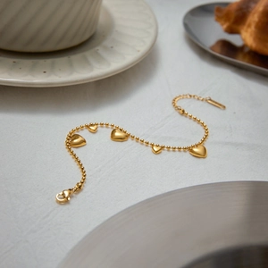 Detail of 18k gold plated stainless steel heart charm bracelet on a white fabric background
