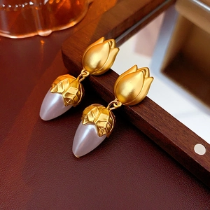 Detail of vintage tulip-shaped gold earrings with white pearl buds on wood