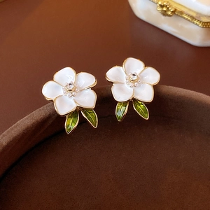 Detailed macro view of enamel flower earrings with pearls and green leaves on brown velvet