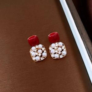 Detail of red square studs and golden frames with white pearls and small rhinestones