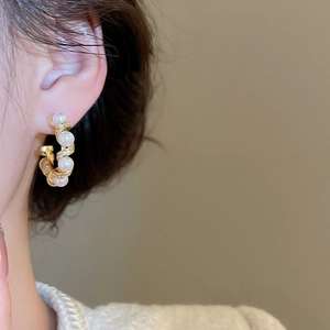 Detail of C-shaped gold-plated hoop earrings with pearls and pavé cubic zirconia studs