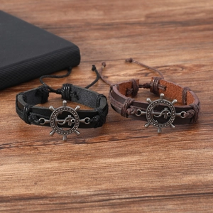 Macro view of woven leather bracelets with metal anchor and rudder charms on wood