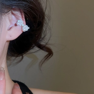 Gros plan d'un ear cuff fleur en zircon argenté avec perles blanches sur une oreille