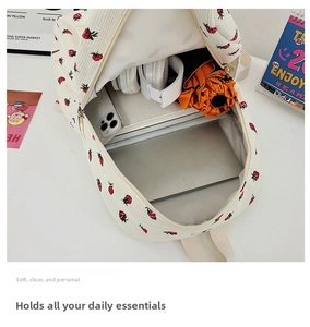 Internal capacity view of white corduroy backpack with strawberry print holding laptop