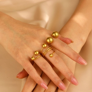 Elegant gold spherical stainless steel rings on silk background worn by a hand