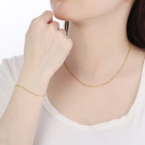 Close-up of a 18K gold snake chain necklace and bracelet on a model wearing white