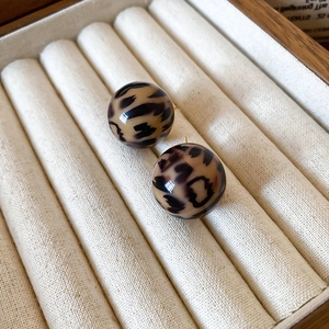 Detailed view of leopard print resin stud earrings in a wooden jewelry display box