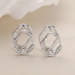 Irregular hollow geometric stud earrings with zircons in silver finish on beige background