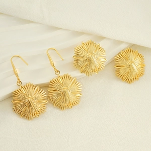 Golden stainless steel flower and bee earrings set shown on a white display stand