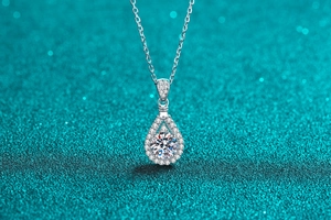 Macro detail of a pear-cut moissanite pendant with halo setting on a silver chain