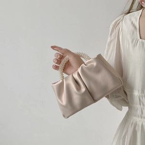 Close-up of beige ruched cloud bag featuring elegant pearl beaded handle on soft fabric