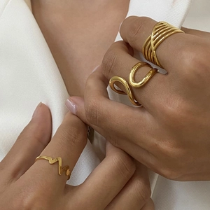Three minimalist gold stainless steel rings in layered, curved, and zigzag designs on a model