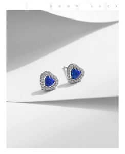 Detail of silver heart halo earrings with blue opal stone on minimalist white background