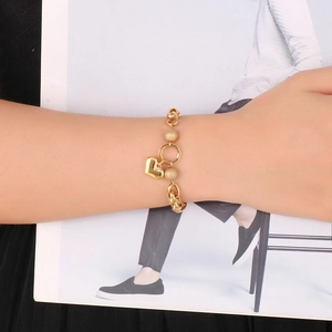 Detail of a gold heart charm bracelet with matte beads worn on a wrist over a magazine