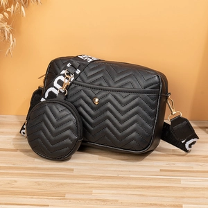 Detail of black V-quilted crossbody bag with gold hardware and wide lettered strap