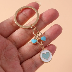 Detail of gold keychain featuring blue heart charms and white round pendant on pink backdrop